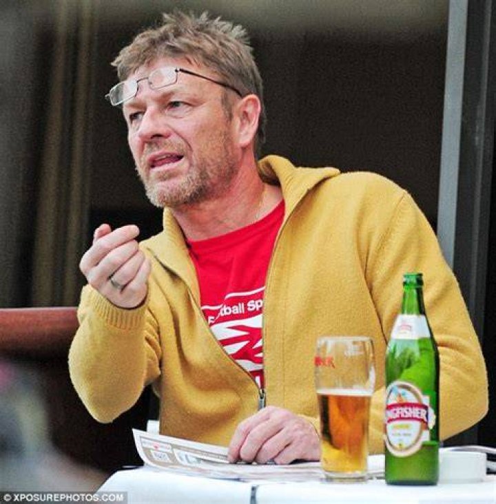 Sean Bean looks disheveled as he sits alone drinking a bottle of lager and smoking cigarettes